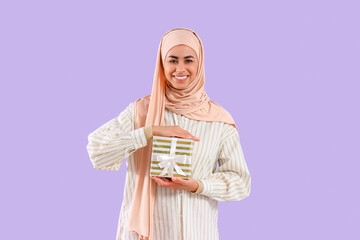 Muslim woman with gift box for Ramadan on lilac background