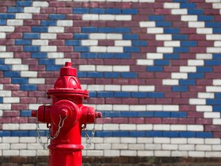 A traditional red fire hydrant in front of a brick wall featuring a classic American pattern in red white and blue - small midwestern town scene at daytime, shallow depth of field.