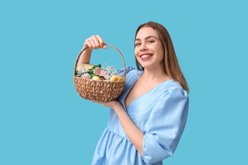 Happy smiling young woman holding basket with makeup products, flowers and Easter decor on blue...
