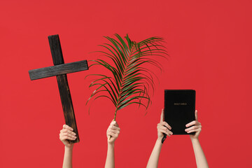 Female hands with wooden cross, palm leaf and Holy Bible on red background. Good Friday concept