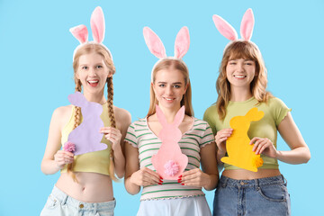 Young girls with Easter bunny ears and paper rabbits on blue background