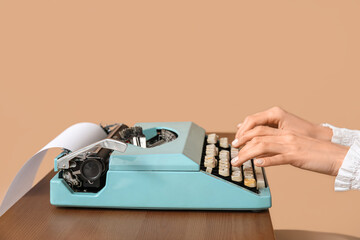 Female hands with vintage typewriter on table against brown background