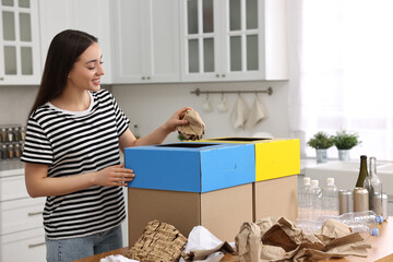 Garbage sorting. Smiling woman throwing crumpled paper into cardboard box in kitchen
