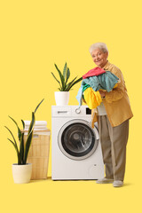 Happy senior woman with heap of clothes doing laundry on yellow background