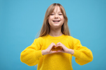 Happy girl showing heart gesture with hands on light blue background