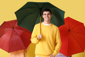 Young people with umbrellas on yellow background