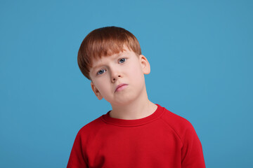 Portrait of sad little boy on light blue background