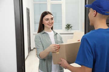 Courier giving parcel to young woman indoors