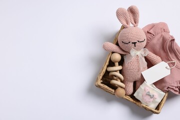 Different baby accessories, clothes and blank card in wicker box on white background, top view....