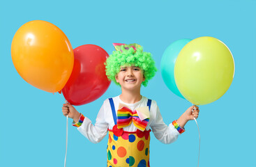 Funny little boy in clown costume with balloons on blue background. April Fools Day celebration