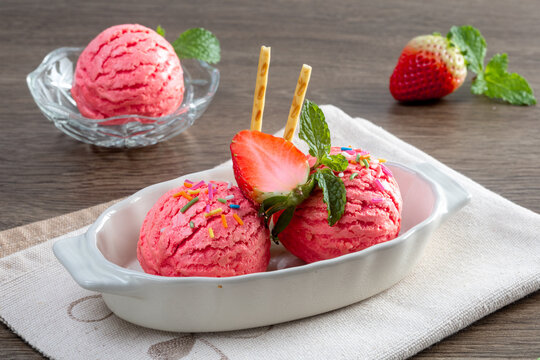Strawberry ice cream in a white bowl with strawberries, napkins on a wooden boards background