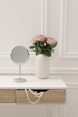 Mirror and vase with pink roses on white dressing table in makeup room