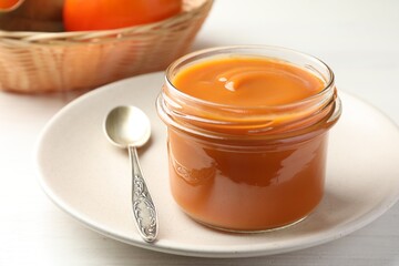 Delicious persimmon jam in glass jar served on white wooden table, closeup