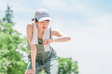 公園でトレーニング・ジョギングのインターバル中にスマートウォッチを確認する若いアジア人女性
