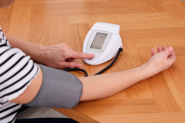 Woman measuring her blood pressure with tonometer at wooden table indoors, closeup