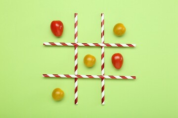 Tic tac toe game made with cherry tomatoes on light green background, top view