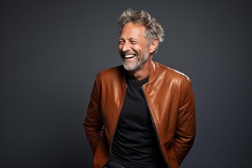 Happy senior man in leather jacket laughing and looking at camera on grey background