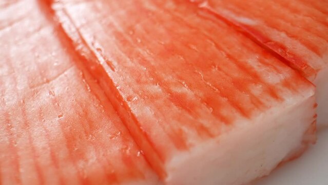 Crab sticks, aka imitation crab or surimi, mimic crab meat in taste, texture, and appearance. They're made from minced white fish like pollock or hake, not actual crab. Processed food concept. 4K.