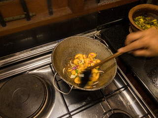 Stirring Round bottom frying pan with stir fry of shrimp on gas burner of stove with warm white overhead lighting