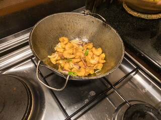 Round bottom frying pan with stir fry of shrimp on gas burner of stove with warm white overhead lighting