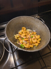 Round bottom frying pan with stir fry of shrimp on gas burner of stove with warm white overhead lighting