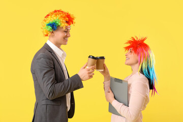Business people in funny wigs with coffee cups on yellow background. April Fools' Day celebration