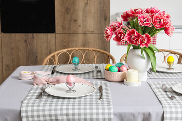 Fototapeta na wymiar Vase with tulips, Easter eggs and dinnerware on dining table in kitchen