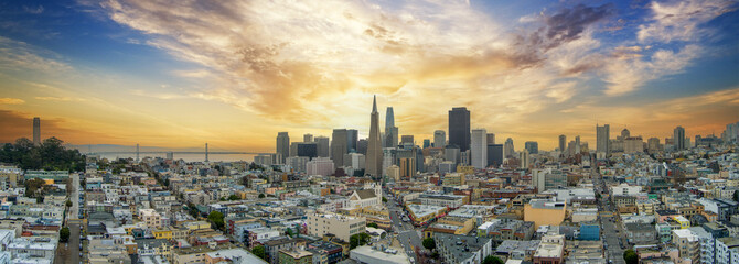 panoramic aerial shot of the ocean and streets lined with apartments, lush green trees and Coit Tower with powerful clouds at sunset in San Francisco California USA