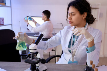 Female African-American chemist working with flask at table in laboratory
