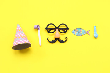 Funny glasses with paper fish party hat and whistle on yellow background. April Fools Day...