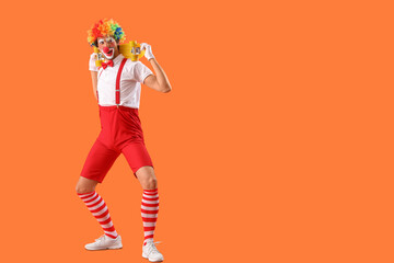 Portrait of funny clown with skateboard on orange background. April Fool's day celebration