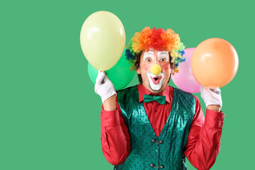 Portrait of surprised clown with balloons on green background. April Fool's day celebration