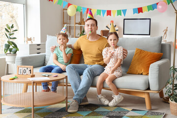 Father and his children with party hats and whistles at home. April Fool's Day celebration