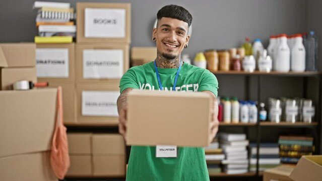 Confident smiling young latin man proudly holding donation package at charity center, volunteering his service in community warehouse