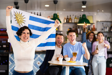Screaming young adult sports fans rooting for favorite team and waving flag of Uruguay while...
