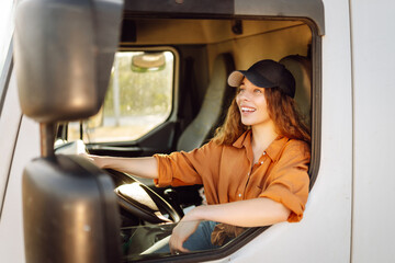 Portrait of beautiful young woman professional truck driver  driving a big truck. Inside of...
