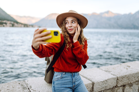 Happy woman in autumn clothes making selfie on smartphone outdoors. Stylish woman with phone. Concept of vacation, technology, weekend.