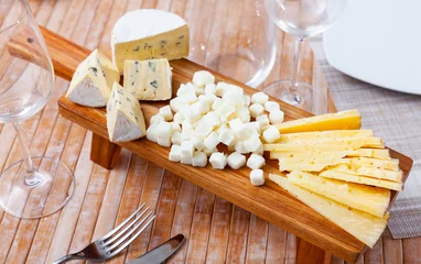 Foto op Plexiglas There is wooden board with cheese variation on table, suitable snack for large company. Cheese slices, blocks and balls will successfully complement low and strong alcoholic beverages © JackF