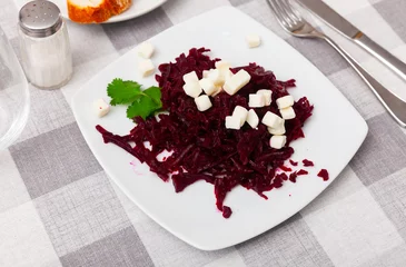 Foto op Plexiglas On plate is portion of salad of grated boiled beetroot with addition of small pieces of white cheese. Dish is decorated with cilantro leaf © JackF