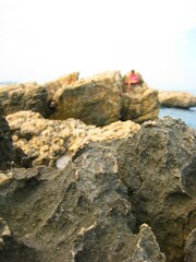 Close up of rocks with cliff, blurred image of man and outdoor nature landscape beach shore ocean coast line background space