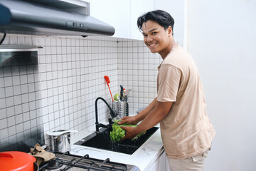 Asian man washing lettuce with water in sink at the kitchen