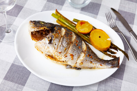Appetizing baked dorada fish served with potatoes and asparagus on platter