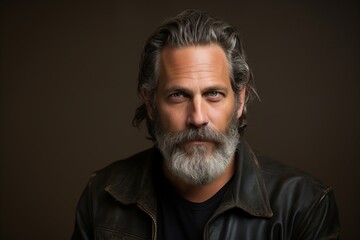 Portrait of a handsome mature man with long gray hair and beard wearing a leather jacket. Men's beauty, fashion.