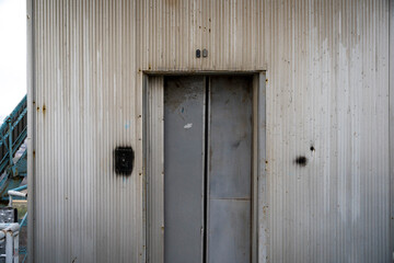  A worn metal door stands against a corrugated wall, its surface telling stories of weathering and time, contrasting textures speaking to industrial aging.
