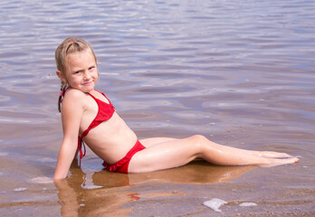 A girl plays on a sandy beach on the shore of a lake in the summer heat.