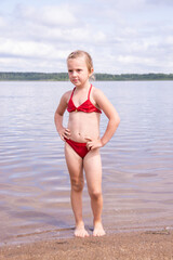 A girl plays on a sandy beach on the shore of a lake in the summer heat.