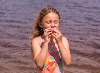 On a hot summer day, a child is relaxing on the lake. A girl on the beach. The girl is holding a pink donut in her hands.