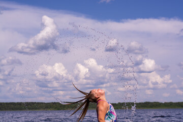 The girl frolics in the water on a hot sunny summer day and is happy.