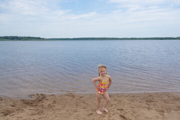 A girl plays on a sandy beach on the shore of a lake in the summer heat.