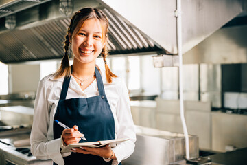 Professional chef's portrait in commercial kitchen. Holding note book pen for teaching. Expertise...